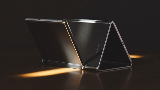 Premium book-style foldable phone in tent pose with a precision-machined silver spine hinge under warm spotlight on a dark walnut surface — editorial hero image for the Galaxy Z Fold 8 vs Motorola Razr Fold case designer's diff